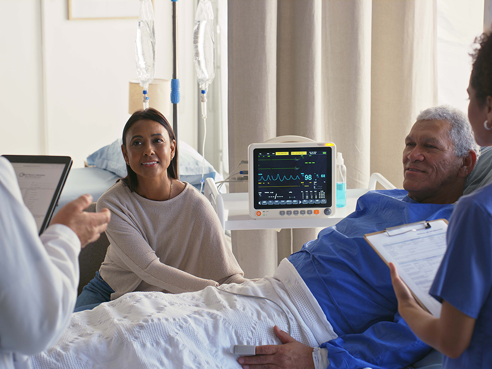 A nurse speaks with a man in a hospital bed, providing language assistance and information about his health.