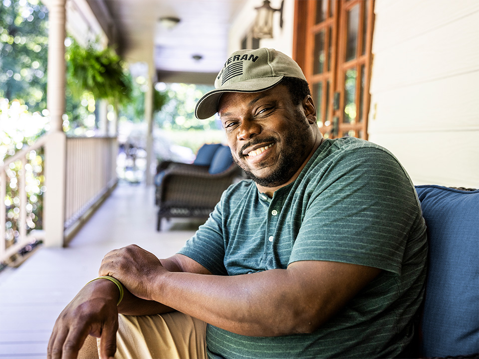 A man in a hat sits relaxed on a porch, enjoying the view and the ambiance of a peaceful outdoor setting.