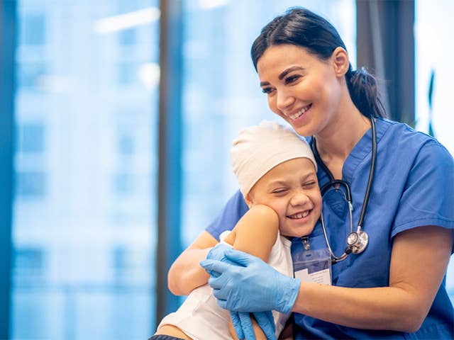 Woman in blue scrubs puts arms around smiling child