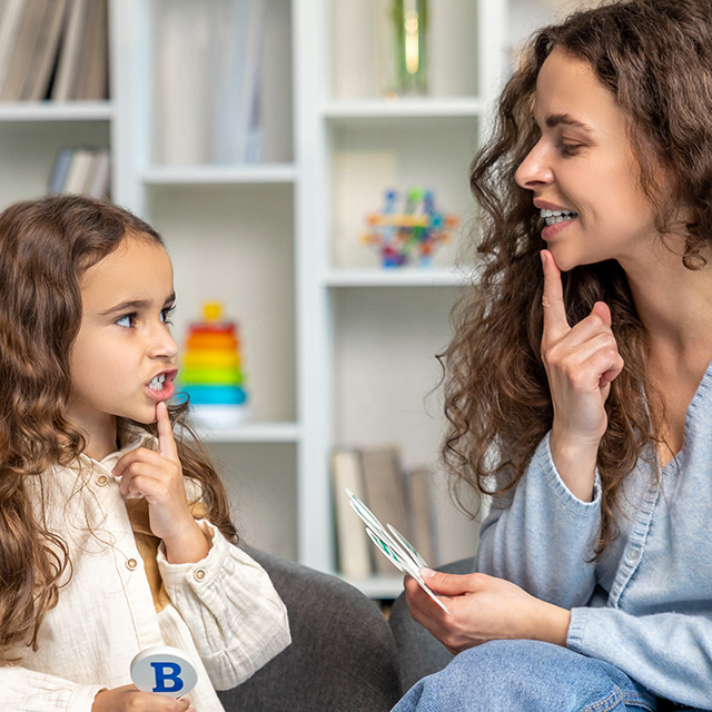 A Corewell Health pediatric speech-language pathologist holds a finger to her chin as she works with a girl in a southeast Michigan clinic