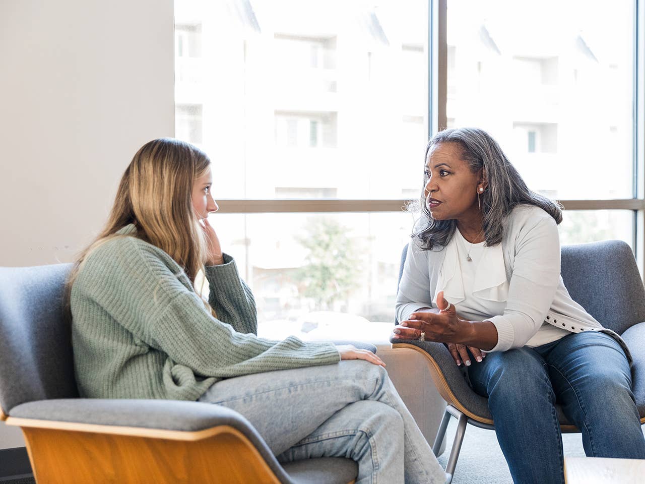 Young woman wearing a light green sweater speaks with a Corewell Health neuropsychologist she is sitting next to in an exam room