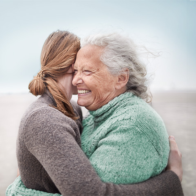 Older Caucasian woman with grey hair hugs a younger woman with brown hair