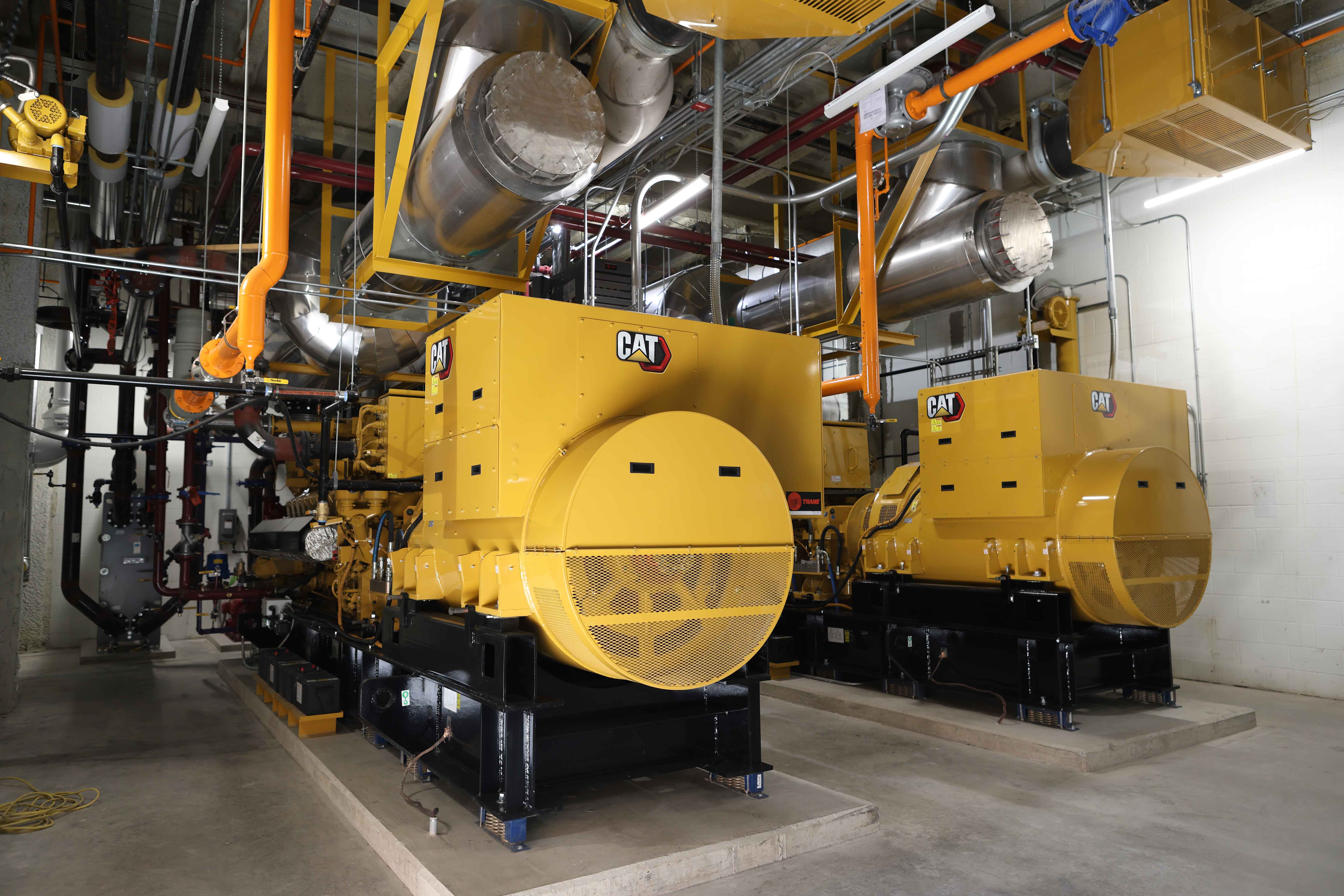 Large yellow electricity generators sitting on cement floor inside a large room