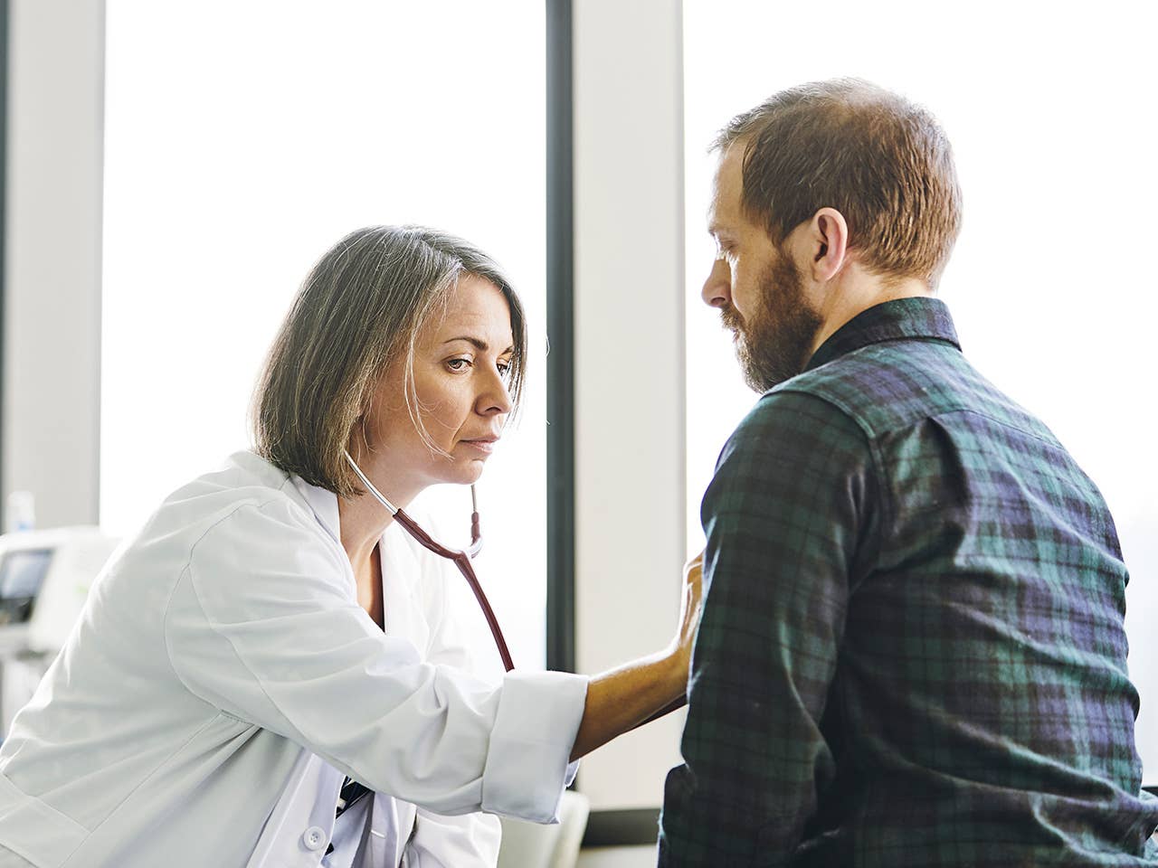 Female doctor in white lab coat uses a stethoscope to listen to a man's heartbeat