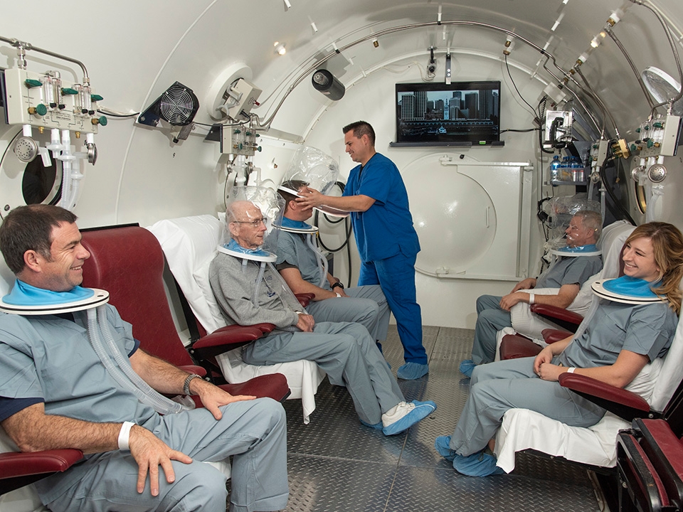 Female patient sits in hyperbaric oxygen chamber wearing an oxygen mask