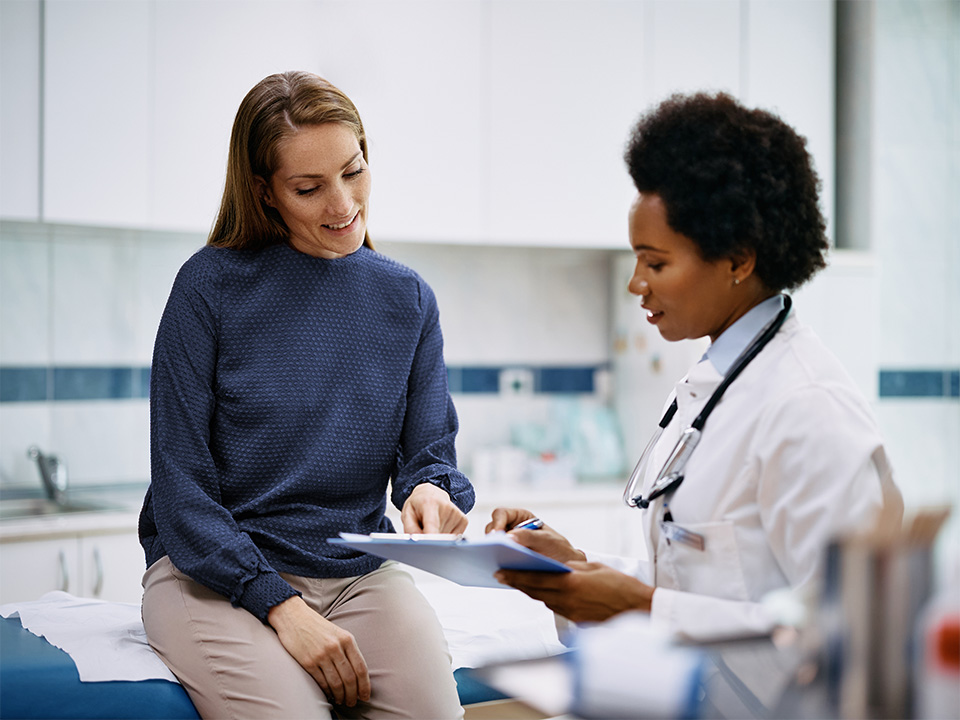 A woman converses with a doctor while seated in a chair during a medical consultation.