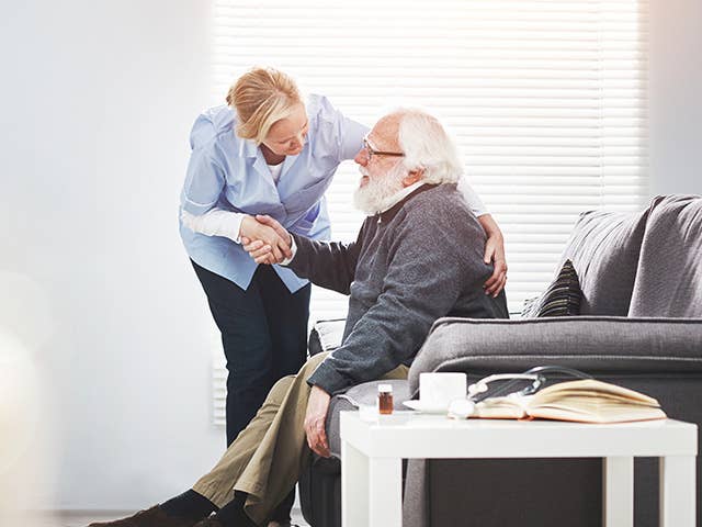 Corewell Health palliative care team member leans over next to an elderly male patient as he sits in a chair