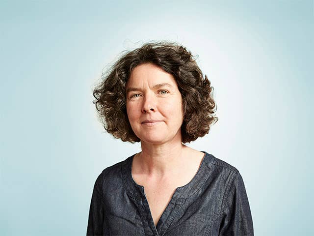 Middle aged white woman with brown hair standing in front of a light blue background
