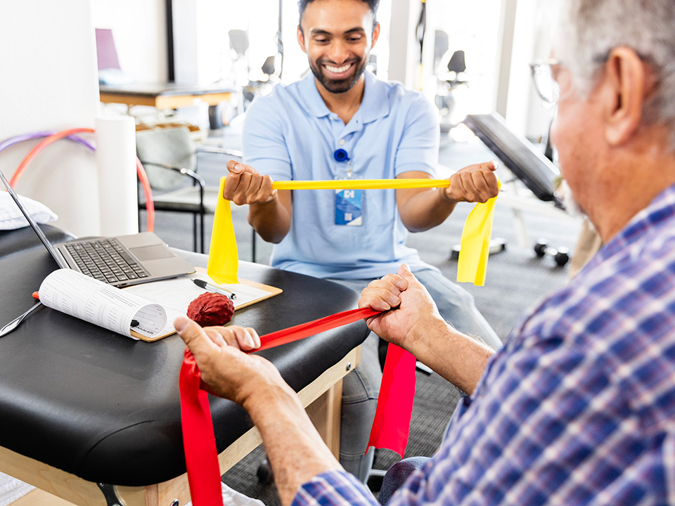 Therapist and male patient stretch large rubber bands in a Corewell Health occupational therapy clinic