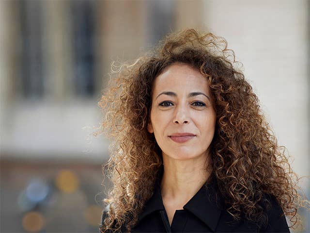 White woman with curly brown hair stands outdoors in front of a building