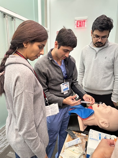 A group of individuals gathers around a mannequin, engaged in a pediatric emergency simulation training session.