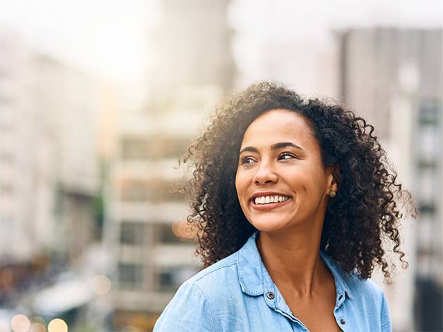 Smiling Black woman in a light blue blouse stands outdoors in a city