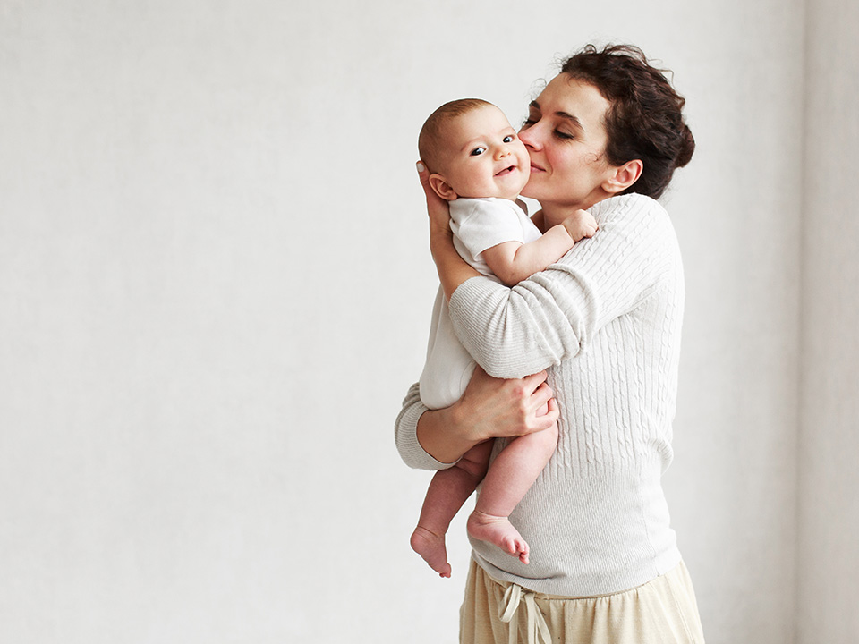 Young mother wearing a white blouse holds her baby and kisses it