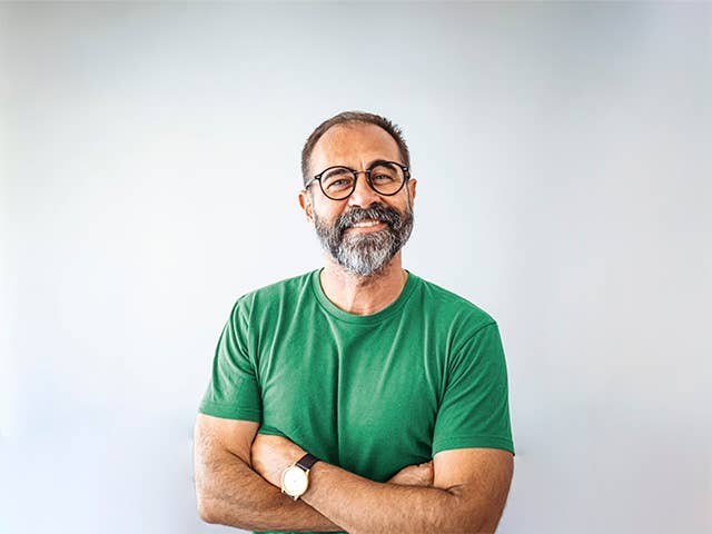 Smiling white man with a grey beard and glasses crosses his arms