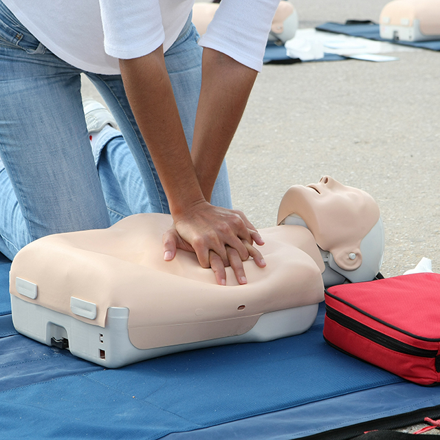 A person performing CPR on a training dummy, demonstrating lifesaving techniques in a practice setting.