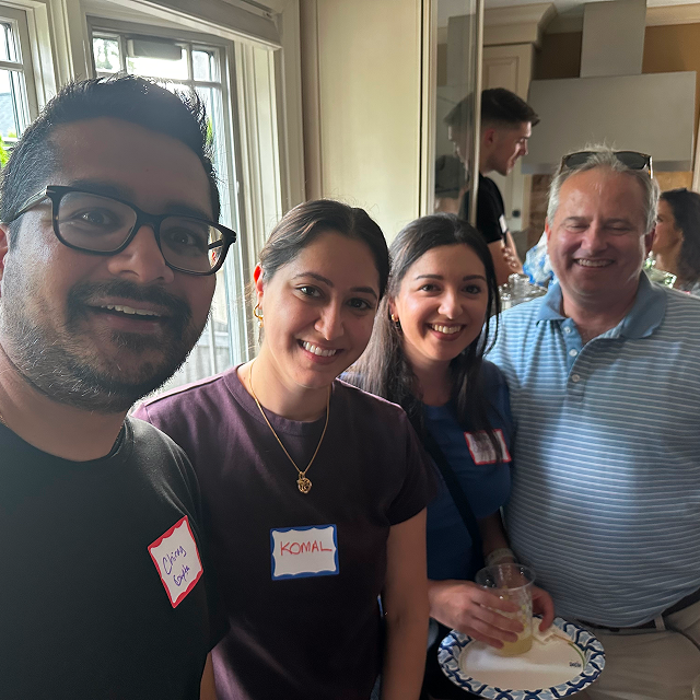 Four attendees wearing name tags pose together indoors at a social gathering.