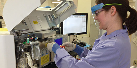 A woman in a lab coat operates a machine, focused on her work in a laboratory setting.