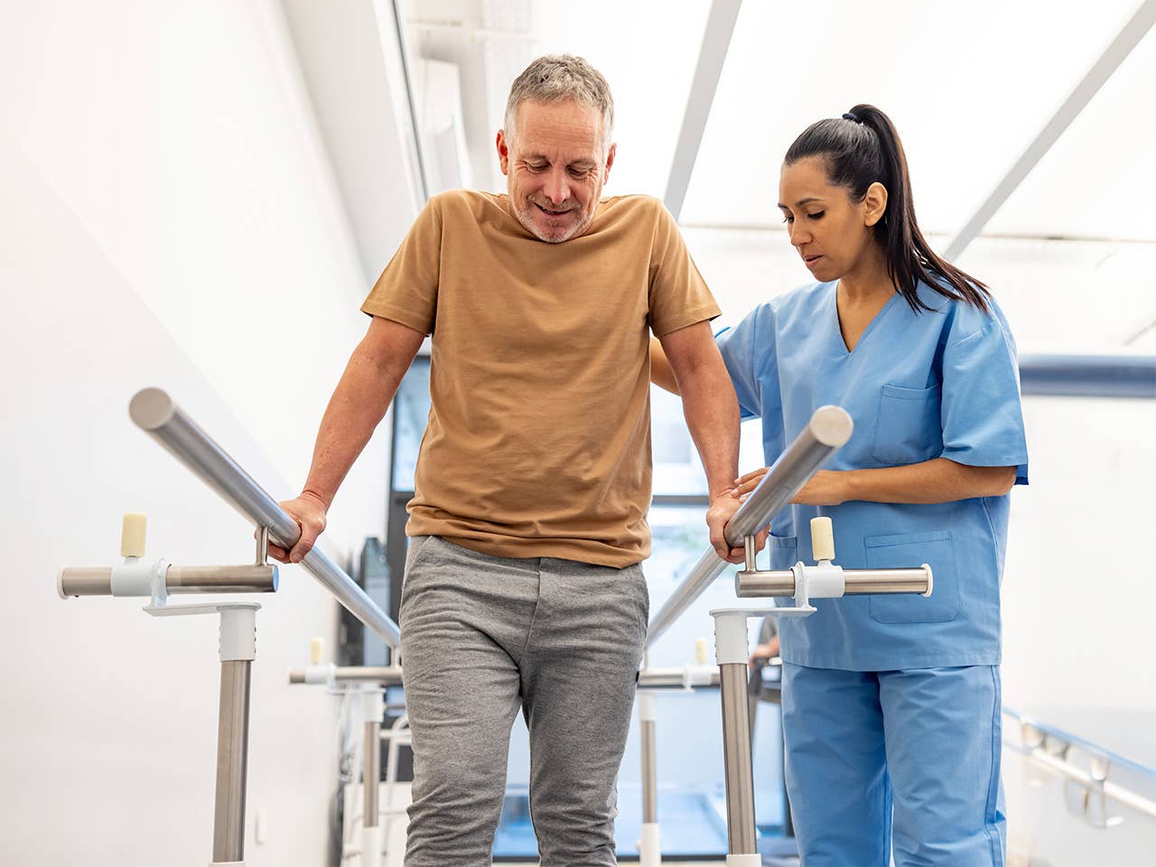 Corewell Health orthopedics rehabilitation team member helps a patient balance with two parallel bars at his side as he stands