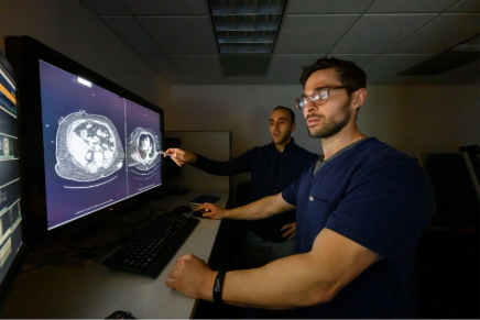 Two men standing in front of a computer screen displaying a large image, engaged in discussion or analysis.