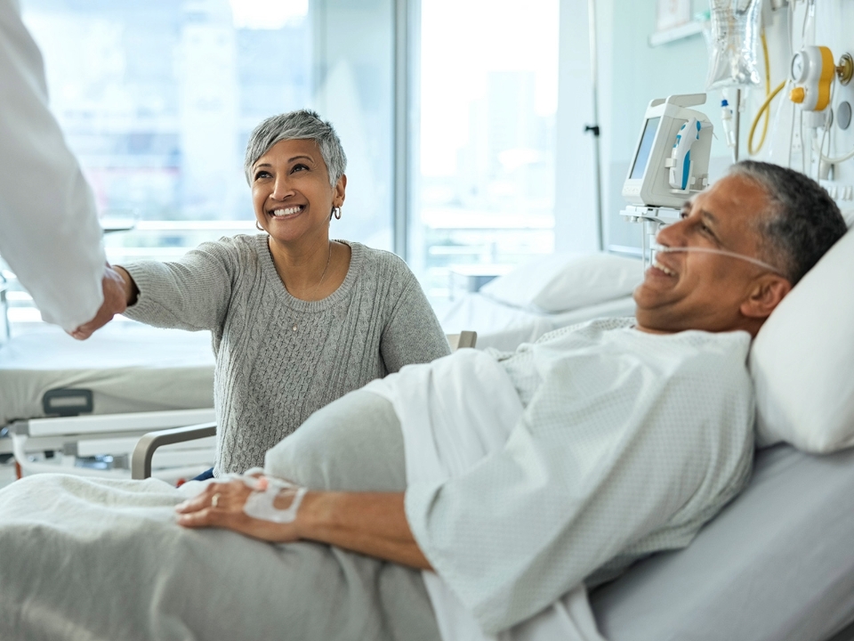 A patients visitor talking to and shaking hands with a doctor in hospital room