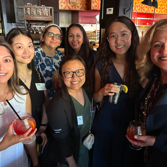 Group of attendees posing together while holding drinks at a residency celebration dinner