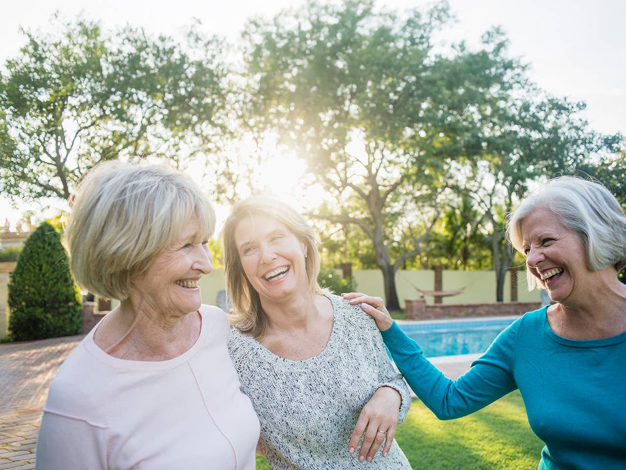 Three older women smile and laugh as they stand together in the evening sunshine
