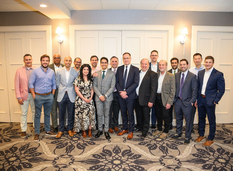 Group photo of a large gathering of people dressed in professional and semi-formal attire standing together in a banquet-style room.