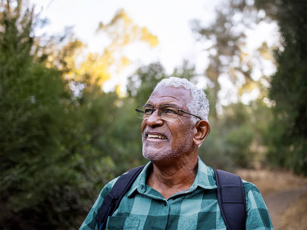 Older Black man looks at the horizon while standing outdoors in a wooded area in the evening