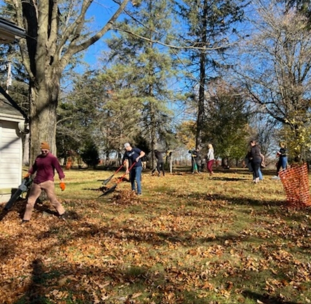 Residents outside raking up leaves on a blue sky fall day