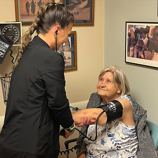 Elderly white woman sits in a chair and holds out her arm as a Corewell Health team member checks her blood pressure
