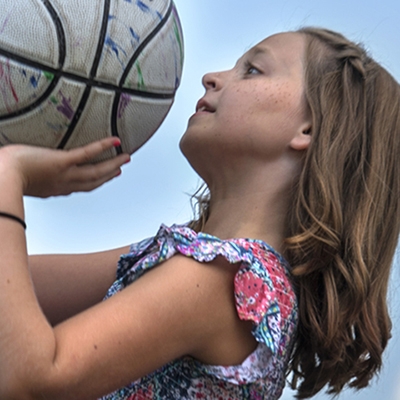 Girl with long brown hair shoots a white basketball