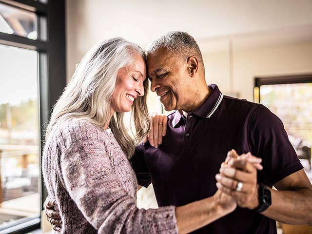 Older man and woman hold hands and smile as they stand face-to-face and dance together