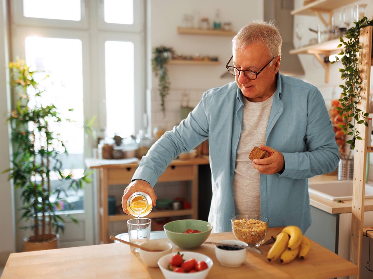 Older adult preparing a nutritious breakfast with fruit, cereal and juice in a home kitchen to support dietary needs.