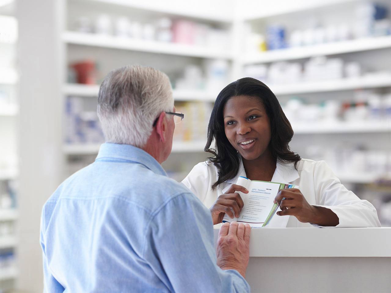 Smiling Corewell Health pharmacist speaks with a male patient at a retail pharmacy counter