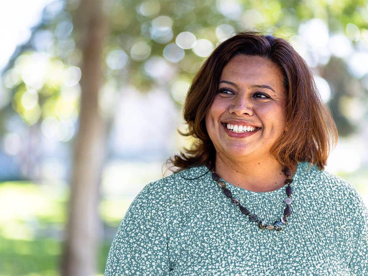 Smiling Black woman stands in the shade of trees outdoors