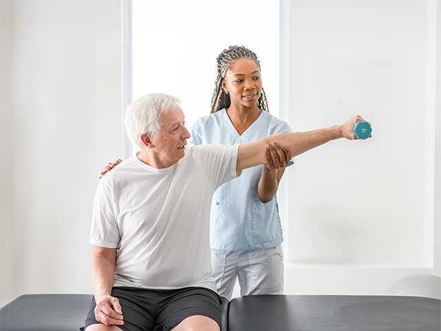 Corewell Health neuro rehab specialist helps an elderly man stretch his arm while holding a weight
