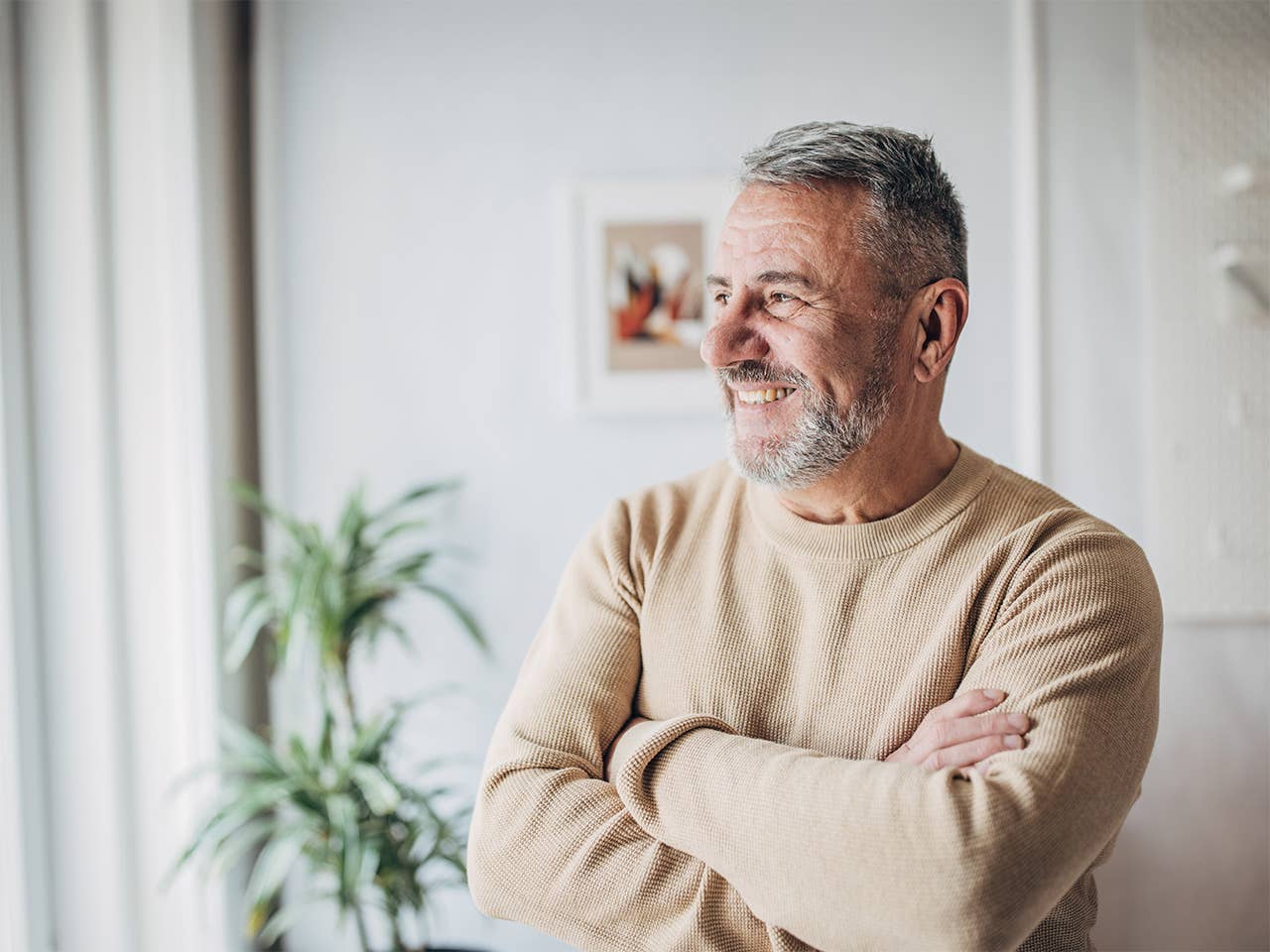 Smiling white man wearing a sweater crosses his arms while looking out a window