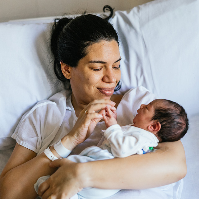 Smiling mother in a hospital bed holding her newborn baby