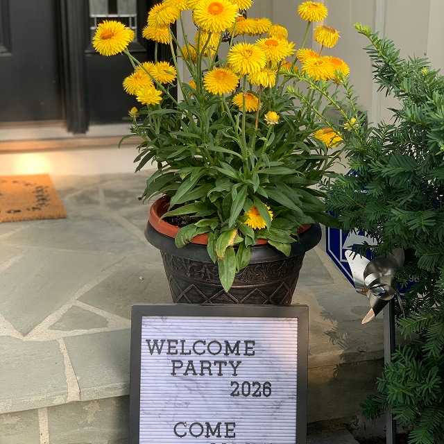 Potted yellow flowers beside a sign welcoming guests to a 2026 welcome party.