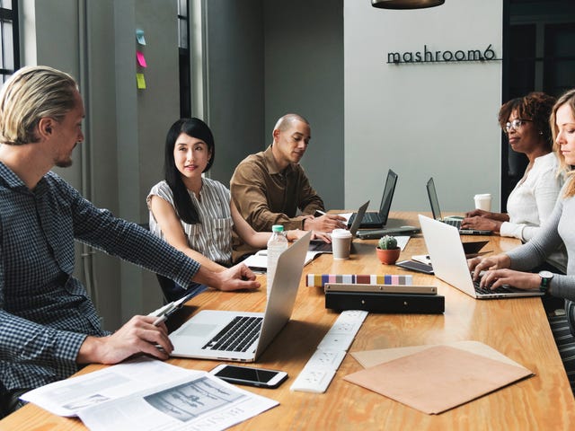 Equipe sentada em uma mesa e cada um esta mexendo em seu computador.