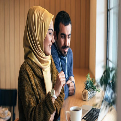 Jovem muçulmana e homem árabe fazendo uma aula online de inglês em uma cafeteria.