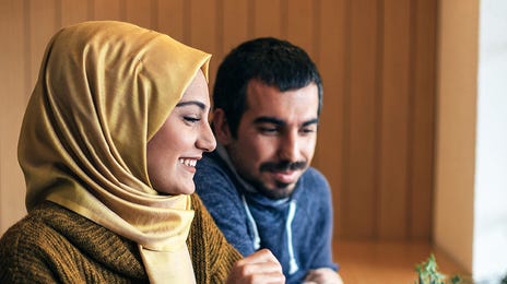 Jovem muçulmana e homem árabe fazendo uma aula online de inglês em uma cafeteria.