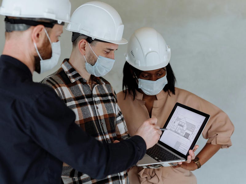 Três profissionais falando inglês para engenheiros ao analisar o cronograma da obra.