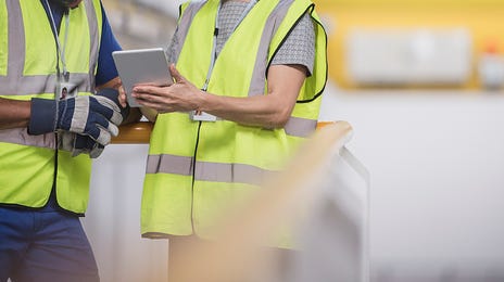 Dois funcionários analisando as diretrizes do carregamento logístico, vestidos com equipamentos de proteção.