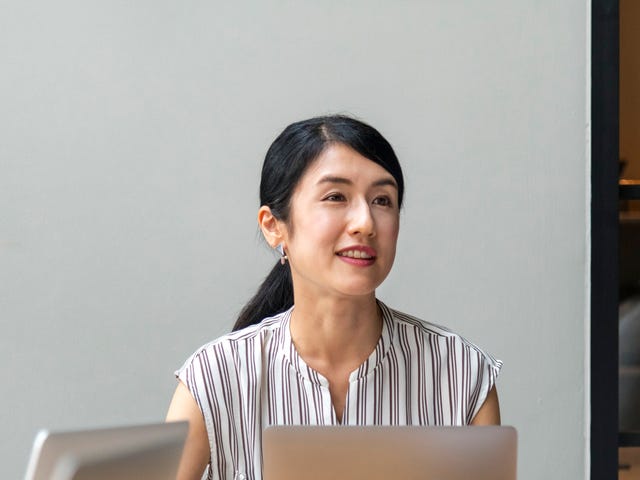 Mulher asiática com um café e seu laptop conversando com sua equipe.