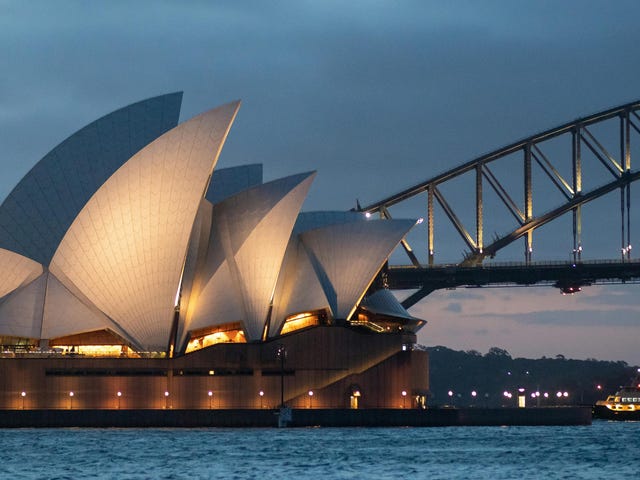 Imagem noturna da atração mais famosa em Sydney na Austrália, com uma ponte ao fundo.