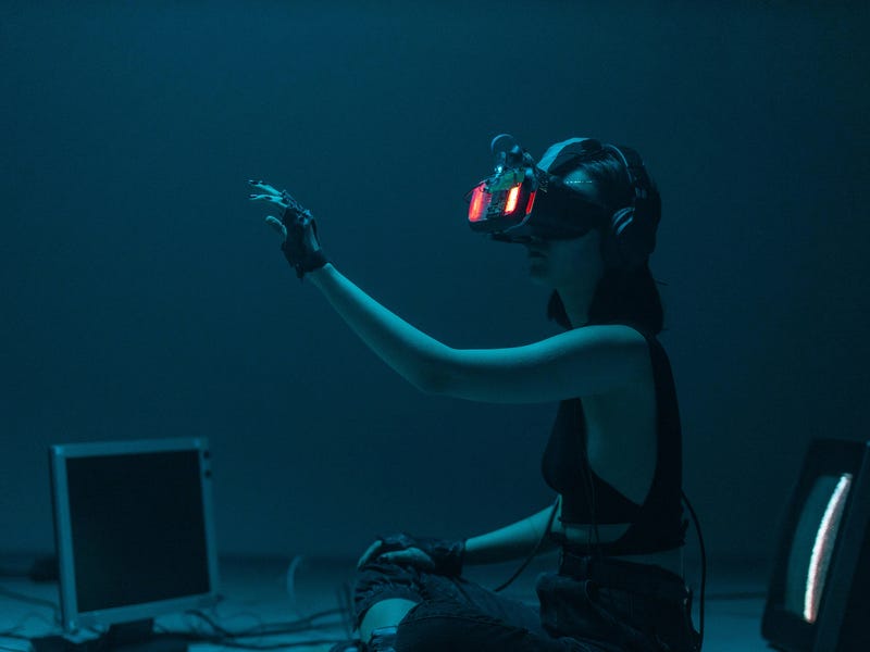 Mulher sentada no chão com computadores e fios ao redor, testando óculos de inteligência artificial.