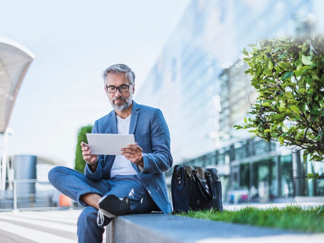 Homem de traje social sentado enquanto tem papéis em mãos.
