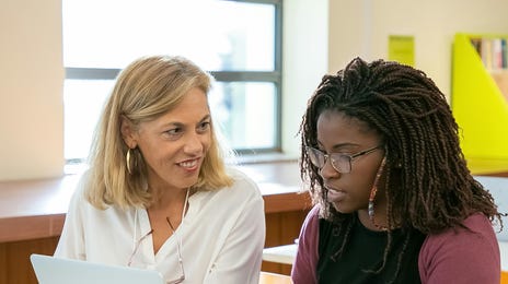 Professora e estudante revisam atividade em classe nas aulas presenciais de idiomas.