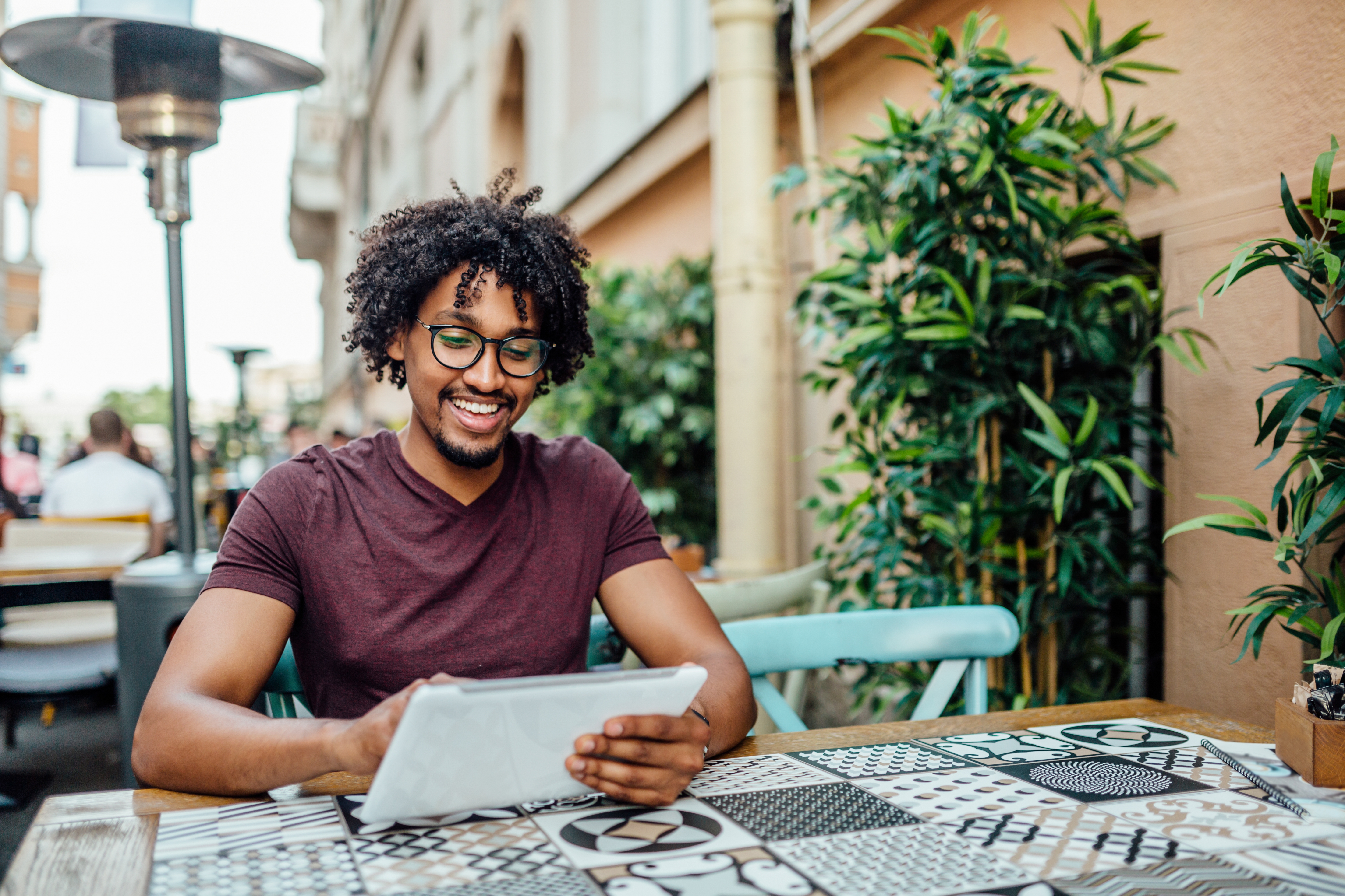 Homem mexendo em um tablet sentado em uma mesa ao ar livre.